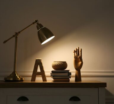 Wooden chest of drawers with books, decor and modern lamp near beige wall
